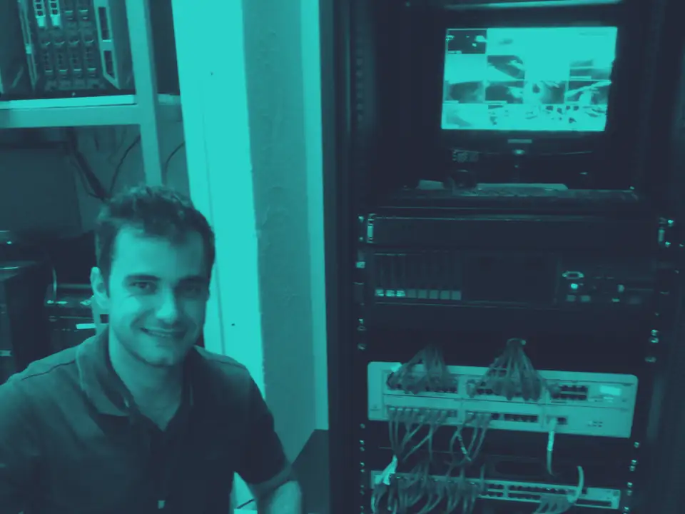Técnico da empresa ao lado de um rack de servidores e switches, com cabeamento de rede organizado