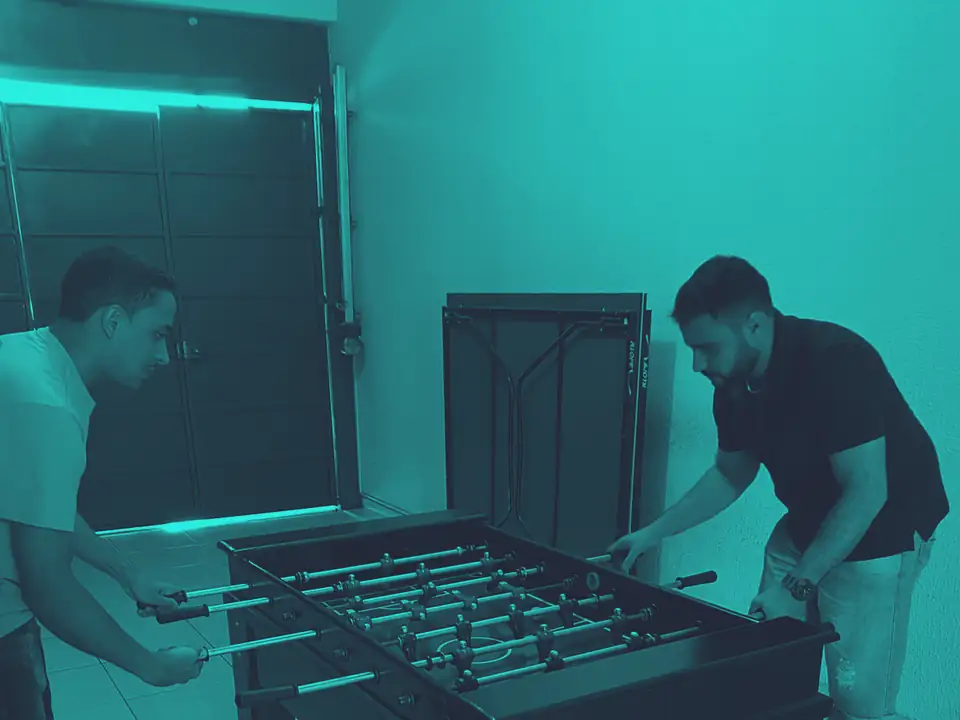 Dois integrantes do time jogando pebolim na sala de jogos da segunda sede