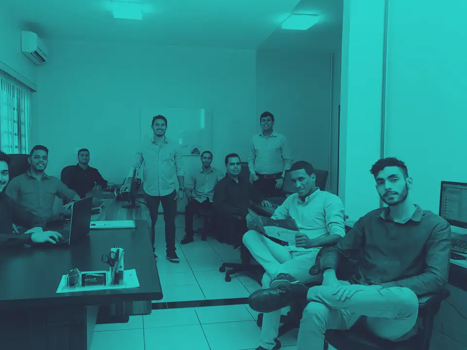 Equipe da DataUnique reunida na sede, sentada e em pé em volta das estações de trabalho